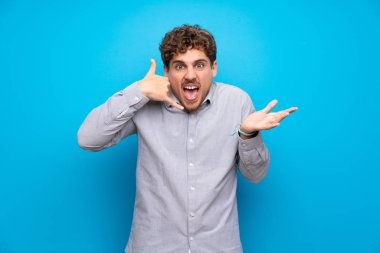 Sarışın adam telefon jest yapma ve şüphe mavi duvarın üzerinden