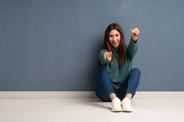 Yerde oturan genç kadın gülümserken seni işaret ediyor.