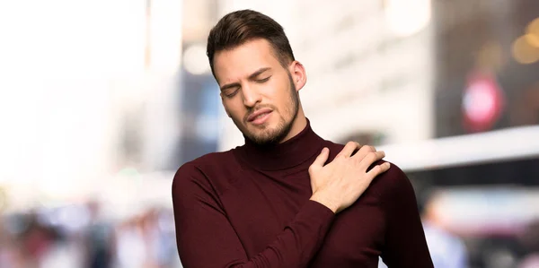 Man with turtleneck sweater suffering from pain in shoulder for having made an effort in the city