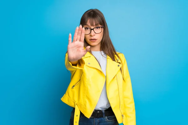 Young woman with yellow jacket on blue background making stop gesture denying a situation that thinks wrong