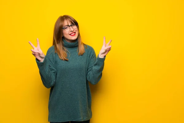 Kadın Gözlük Gülümseyen Iki Elini Zafer Işaretiyle Gösterilen Sarı Duvarın — Stok fotoğraf