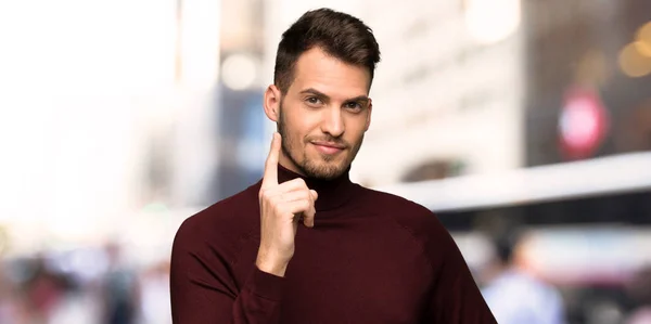 Man with turtleneck sweater showing and lifting a finger in sign of the best in the city