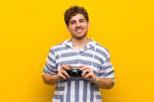 Homem Loiro Sobre Parede Amarela Segurando Uma Câmera — Fotografia de Stock