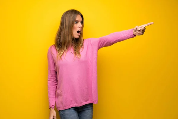 Mujer Con Suéter Rosa Sobre Pared Amarilla Apuntando Hacia Afuera —  Fotos de Stock