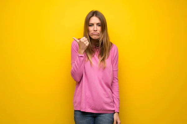 不幸とポインティング側に黄色の壁にピンクのセーターの女性 — ストック写真