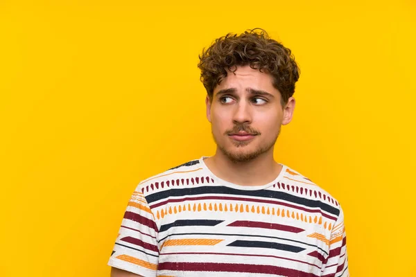 Blonde man over yellow wall standing and looking to the side