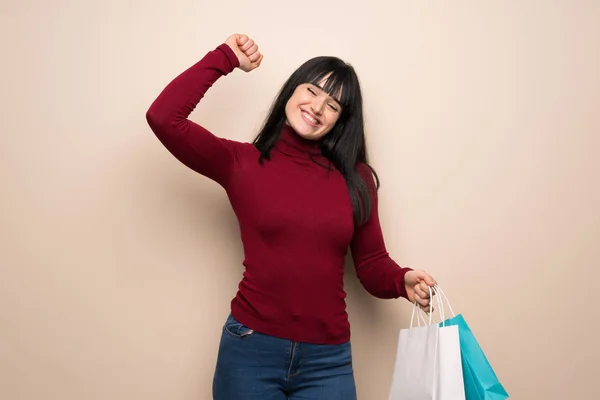 Young woman with red turtleneck holding a lot of shopping bags in victory position