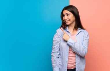 Pembe ve mavi duvar tarafına işaret eden bir ürün sunmak için genç kadın