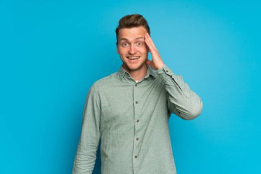 Sürpriz ve şok yüz ifadesi ile izole mavi duvarın üzerinden sarışın adam