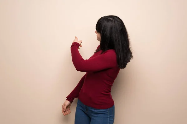 Young woman with red turtleneck pointing back with the index finger