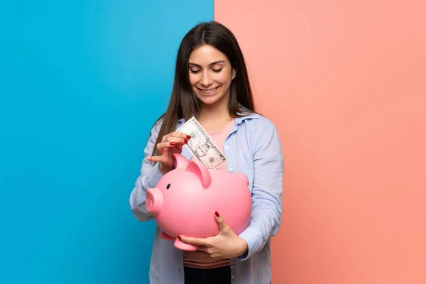 Jovem Mulher Sobre Parede Rosa Azul Tomando Banco Porquinho Feliz — Fotografia de Stock