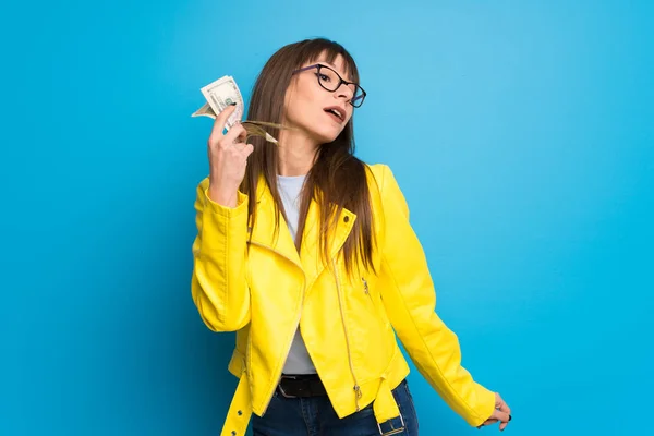 Young woman with yellow jacket on blue background taking a lot of money