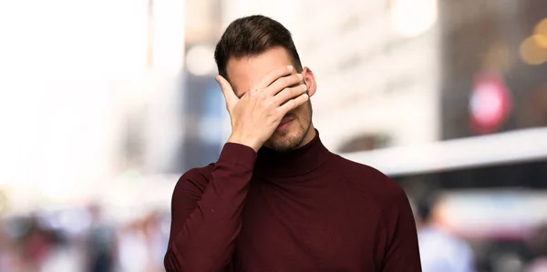 Man with turtleneck sweater covering eyes by hands. Do not want to see something in the city