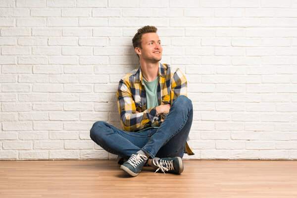 Сидящий на полу блондин счастлив и улыбается
