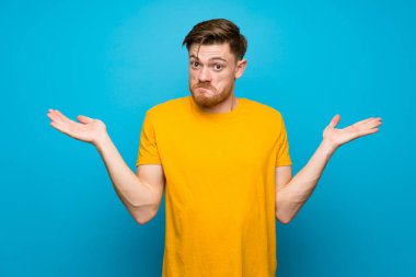 El kaldırırken şüpheleri olan mavi duvarın üzerinde kızıl saçlı adam