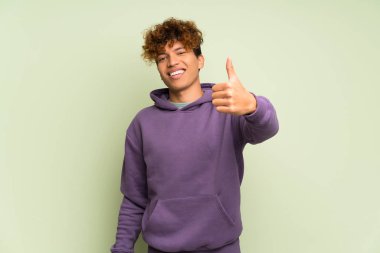 Genç Afro-Amerikan adam, yeşil duvarın üstünde. Başparmakları yukarıda. Çünkü iyi bir şey oldu.