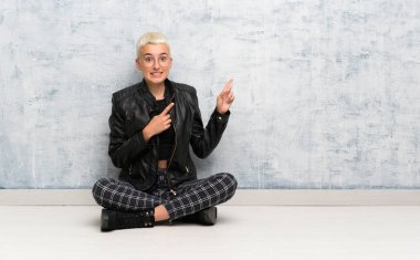 Yerde oturan genç bir kadın bir ürün sunmak için yan tarafı işaret ediyor.