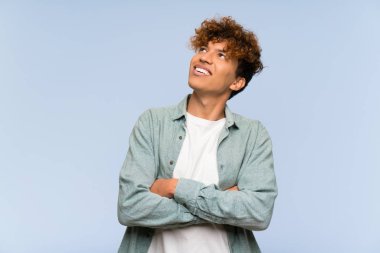 Genç Afro-Amerikan adam mavi duvarın ardında gülümserken yukarı bakıyor.