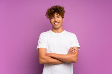 İzole edilmiş mor duvarın üzerinde kollarını ön cephede birleştiren genç Afro-Amerikan bir adam var.