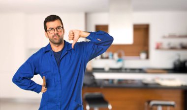 Evde negatif ifade ile başparmak aşağı işareti gösteren ressam adam