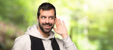 Spor adam bir parkta kulak el koyarak bir şey dinliyor