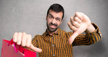 Dokulu duvar üzerinde her iki eliyle başparmak aşağı gösteren alışveriş çantaları ile adam