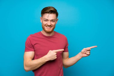 Izole mavi duvarda kızıl saçlı adam yan parmak işaret