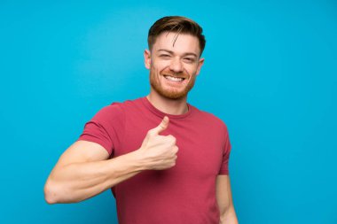 Izole mavi duvarda Redhead adam jest kadar bir başparmak veren