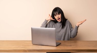 Dizüstü bilgisayarıyla çalışan genç bir kadın telefon hareketinde bulunuyor.