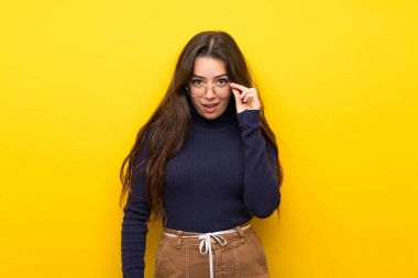 Gözlük ile izole sarı duvar üzerinde genç kız ve sürpriz