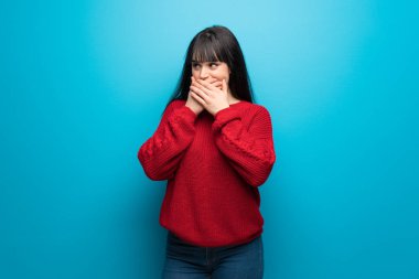 Mavi duvarın üstünde kırmızı kazaklı bir kadın ağzını kapatıp yan tarafa bakıyor.