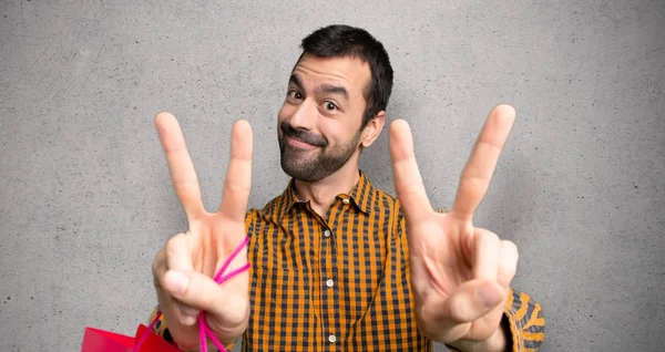 Hombre Con Bolsas Compras Sonriendo Mostrando Signo Victoria Con Ambas —  Fotos de Stock