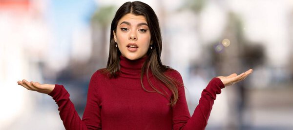 Teenager girl with turtleneck having doubts while raising hands at outdoors