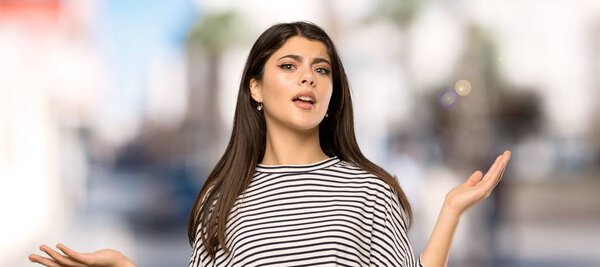 Teenager girl with striped shirt unhappy because not understand something at outdoors