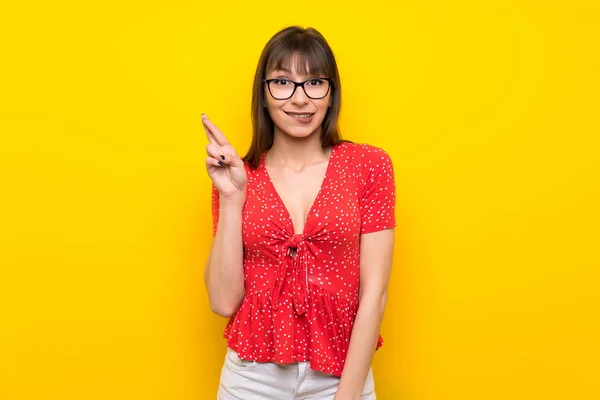 Young woman over yellow wall with fingers crossing and wishing the best