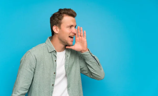 Blonde handsome man with green shirt shouting with mouth wide open