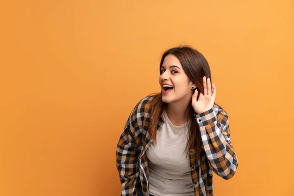 耳に手を置くことによって何かを聞いている茶色の壁の上の若い女性 — ストック写真