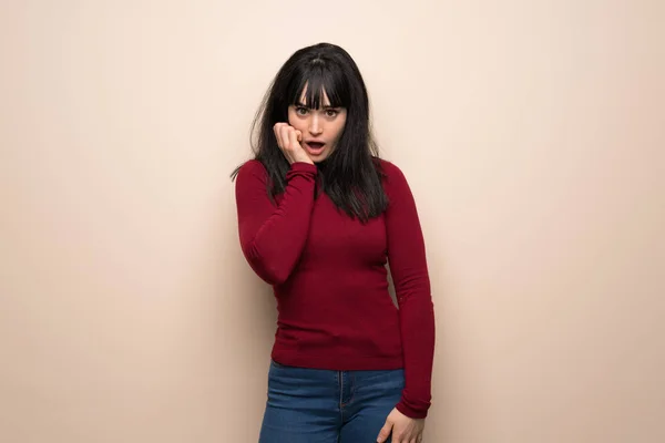 Young woman with red turtleneck surprised and shocked while looking right