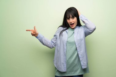 Yeşil duvarın üstünde genç bir kadın var. Parmakla işaret ediyor ve bir ürün sunuyor.