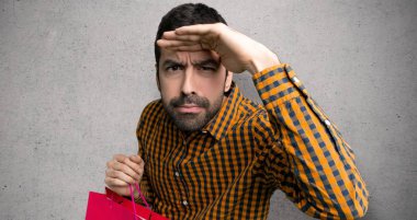 Alışveriş çantaları ile adam uzak dokulu duvar üzerinde bir şey bakmak için el ile bakıyor