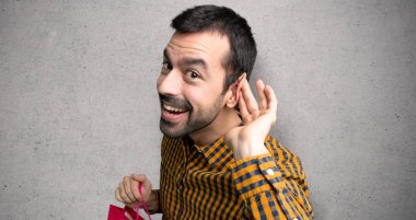 Adam alışveriş çantaları ile dokulu duvar üzerinde kulak el koyarak bir şey dinlerken