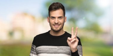 Yakışıklı adam gülümseyen ve açık havada zafer işareti gösteren