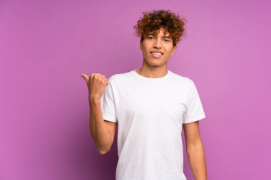 İzole edilmiş mor duvarın üzerinde genç bir Afro-Amerikan erkeği bir ürünü sunmak için kenarı işaret ediyor.