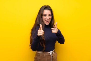 Genç kız üzerinde izole sarı duvar öne işaret ve gülümseyen