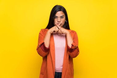 Sarı duvarın arkasındaki genç Kolombiyalı kız sessizlik işareti gösteriyor.