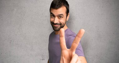 Yakışıklı adam gülümseyen ve dokulu duvar üzerinde zafer işareti gösteren