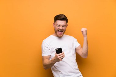 Zafer pozisyonunda telefon ile kahverengi duvar üzerinde Redhead adam