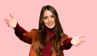Ceket sunan ve izole pembe arka plan üzerinde el ile gelmek için davet ile genç kadın