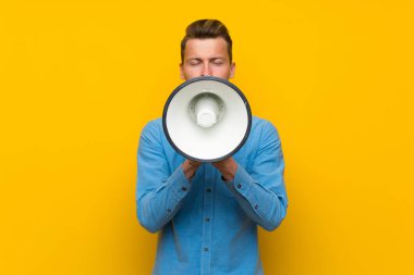 Bir megafon üzerinden bağıran izole sarı duvar üzerinde sarışın adam
