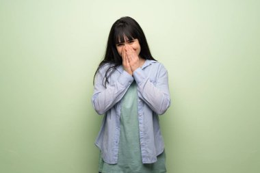 Yeşil duvarın ardında ağzı kapalıyken gülümseyen genç bir kadın.